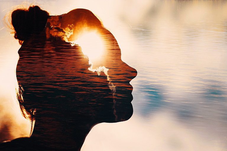 Silhouette of a person with a sunset and water scene blending inside.