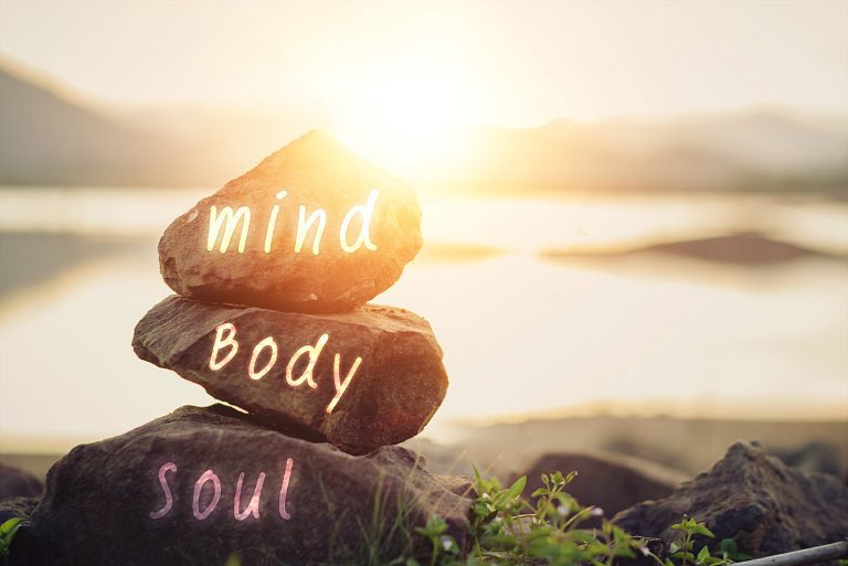 Stacked stones labeled mind, body, soul at sunrise, symbolizing balance.
