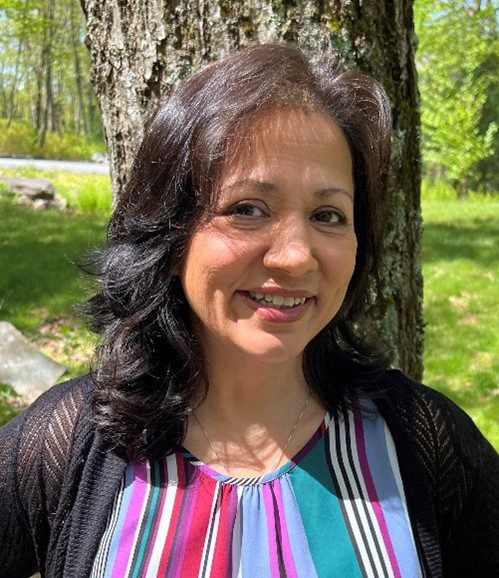 Smiling woman outdoors with sunlight and greenery.